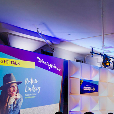 photo: woman presenting on stage with background graphics at corporate event